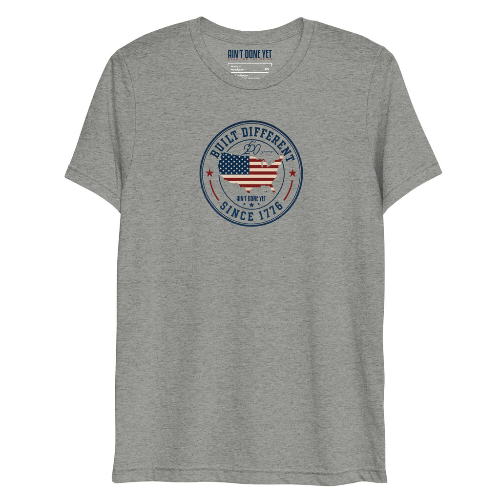 Built Different America 250 athletic grey tri-blend t-shirt featuring patriotic circular emblem with American flag and 1776 design.