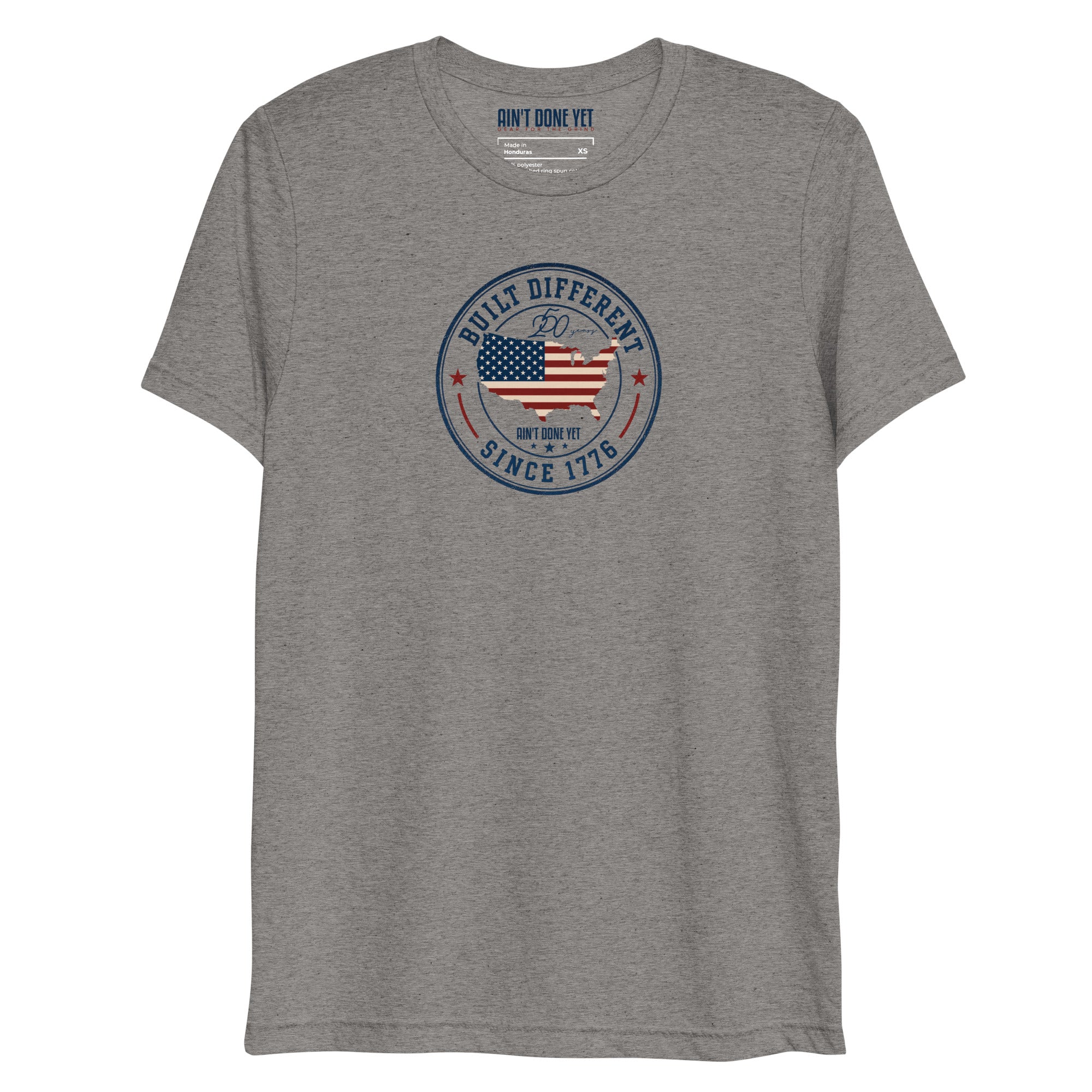 Built Different America 250 grey tri-blend t-shirt featuring patriotic circular emblem with American flag and 1776 design.