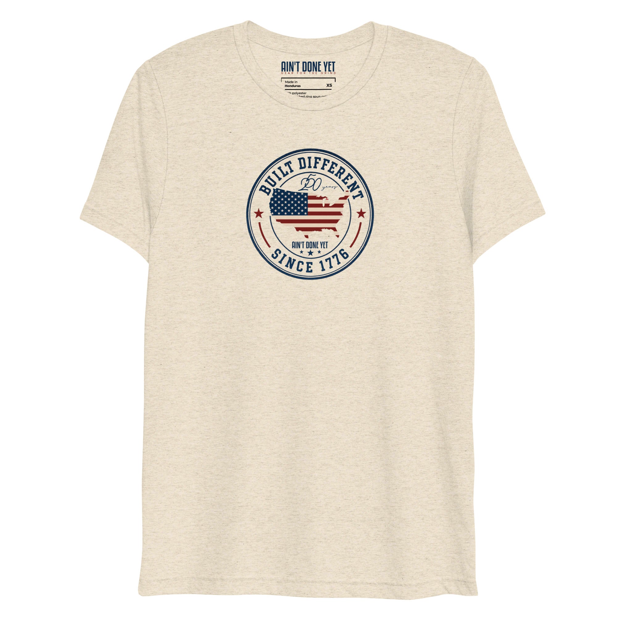 Built Different America 250 oatmeal tri-blend t-shirt featuring patriotic circular emblem with American flag and 1776 design.