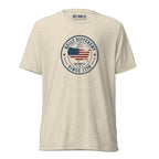 Built Different America 250 oatmeal tri-blend t-shirt featuring patriotic circular emblem with American flag and 1776 design.