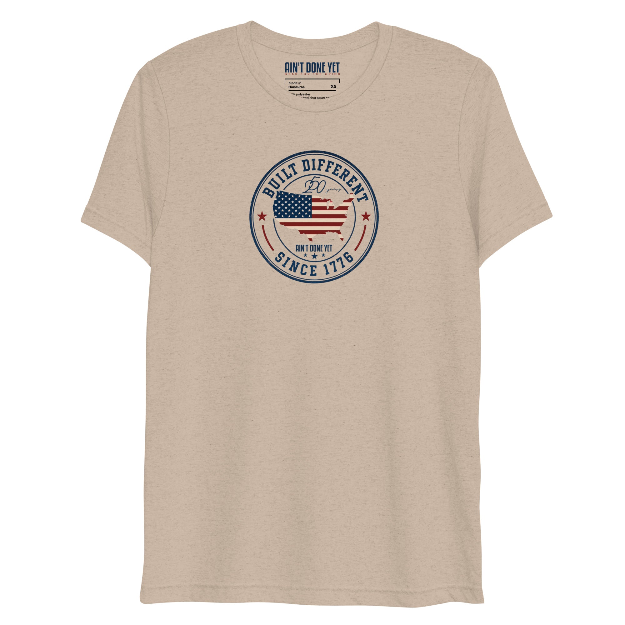 Built Different America 250 tan tri-blend t-shirt featuring patriotic circular emblem with American flag and 1776 design.