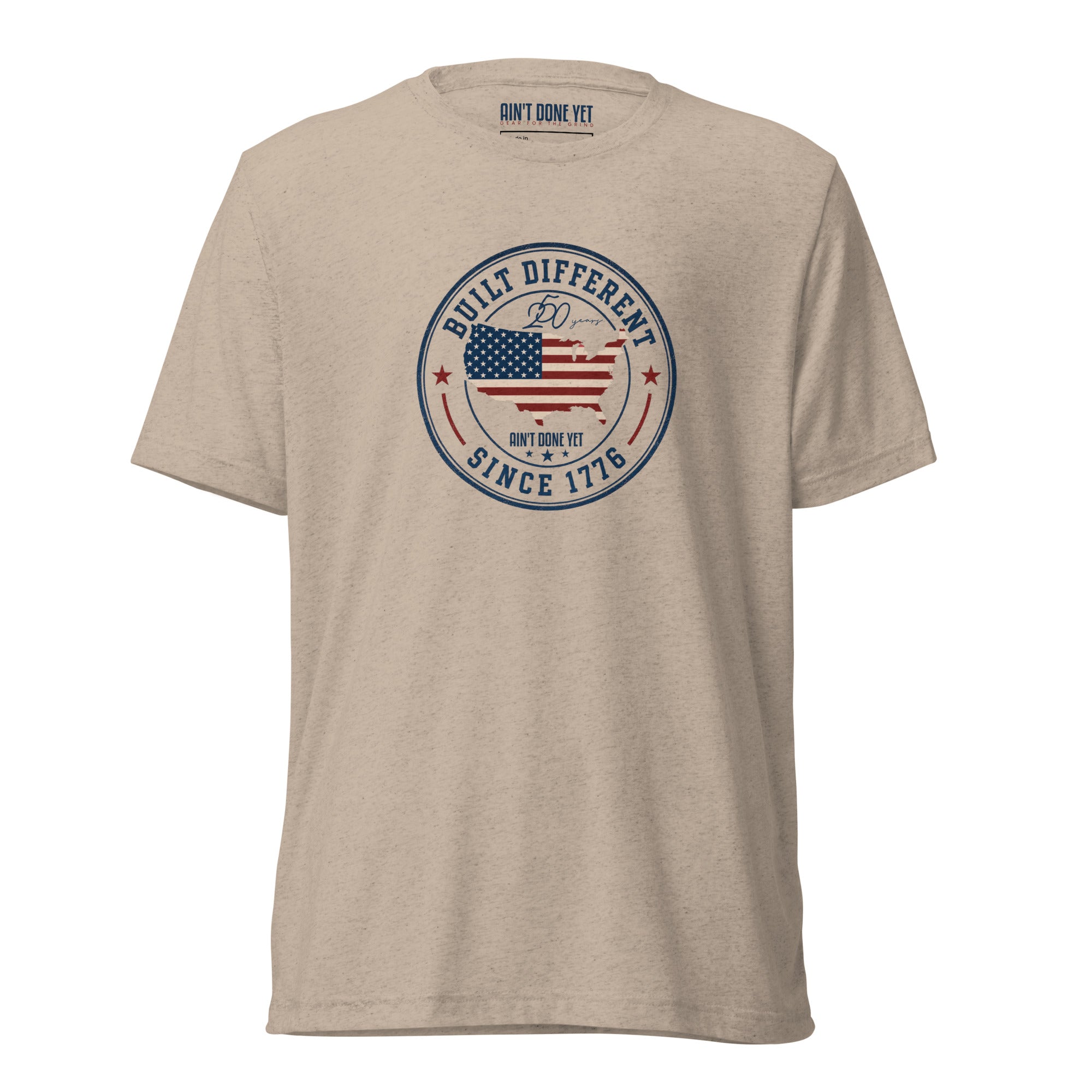 Built Different America 250 tan tri-blend t-shirt featuring patriotic circular emblem with American flag and 1776 design.