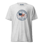 Built Different America 250 white fleck tri-blend t-shirt featuring patriotic circular emblem with American flag and 1776 design.